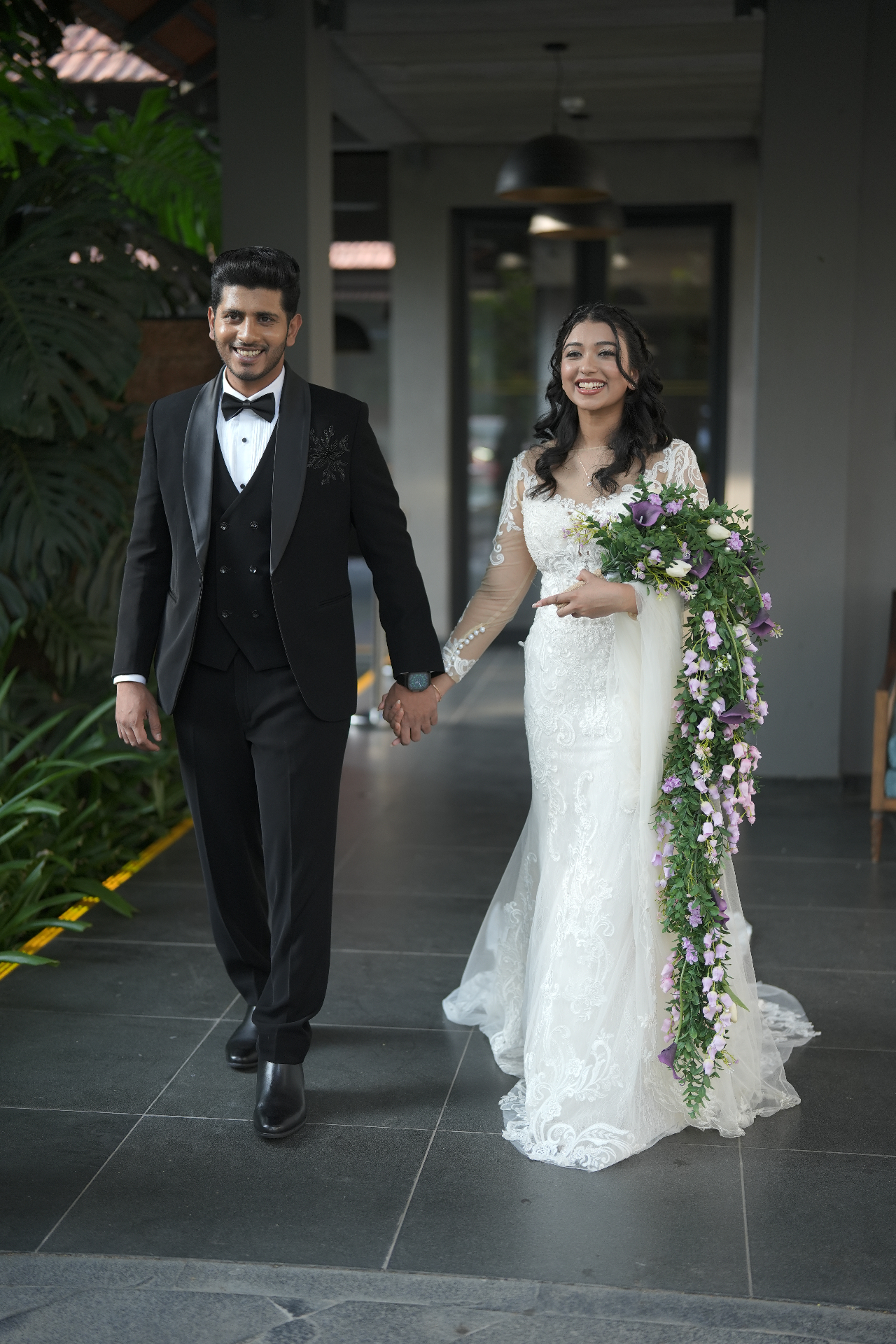 Bride in lace gown with cascading bouquet beside groom in black tuxedo